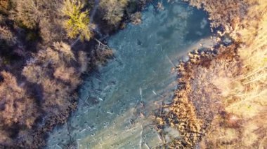 Sıcak günbatımında, ormanda, donmuş küçük vahşi göl üzerinde, kış manzarasının üzerinde uçan hava spiral hızı. Kışın güneşli, mavi, buzlu gölete bak.