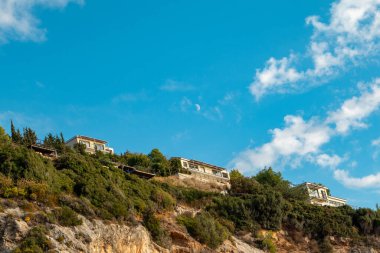 Yunanistan 'ın Lefkada adasında yeşil yüksek tepelerde, mavi gökyüzünde, bulutlu ve genç aylı konak evleri ile manzaralı canlı bir manzara. Yazın seyahat.