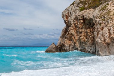 Beyaz köpüklü gök mavisi dalgalar kayalık kıyıları kırıyor. Yunanistan 'ın Lefkada adasında gökyüzü dramatik bulutlu Mylos plajı. Yaz doğası İyon Denizi 'ne seyahat