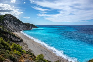 Lefkada adasının yeşil kayalık kıyılarında gök mavisi renkli dalgalar. Yunanistan 'da destansı bulutlu Mylos kumlu plajı. İyon Denizi 'ne yaz tatili