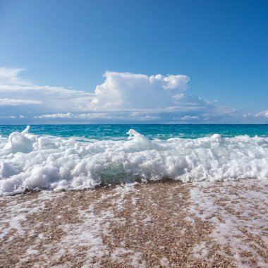 Yunanistan 'ın Lefkada adasında dalgalar ve destansı bulutlarla dolu çakıl taşlı sahilde parlayan beyaz köpük damlası. İyon Denizi 'nin Yaz Doğası
