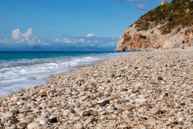 Yunanistan 'ın Lefkada adasının kıyısında masmavi deniz, beyaz köpük ve kayalık kayalıklı güneşli mavi Mylos çakıl taşı plajı. İyon Denizi 'ne yaz tatili