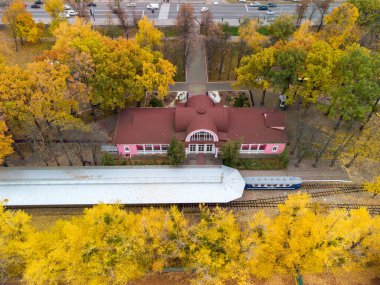 Fly above Children's Southern Railway Station. Track line and platform with train in vivid yellow autumn trees. Aerial treetop view on colorful Kharkiv, travel Ukraine