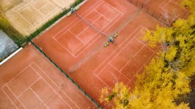 Şehir parkındaki turuncu kil tenis kortlarının üzerinden uç. Canlı sarı sonbahar yaprakları spor eğlence alanına düşüyor. Renkli Kharkiv 'de havadan ağaç manzarası, Ukrayna seferi