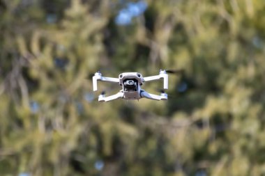 Kharkiv, Ukrayna - 6 Mart 2021: Dji Maviç Mini 2 insansız hava aracı, güneşli ormanda uçuyor. Bulanık yeşil arkaplan üzerinde gezinen yeni dörtlü helikopter aygıtı
