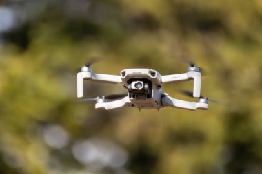 Kharkiv, Ukrayna - 6 Mart 2021: Dji Maviç Mini 2 insansız hava aracı, güneşli ormanda uçuyor. Bulanık yeşillik arkaplanı olan yeni dörtlü helikopter aygıtı