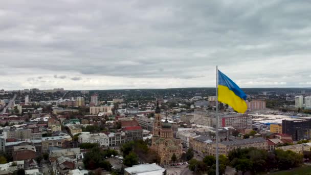 乌克兰的黄色和蓝色旗帜在旗杆上迎风飘扬 有着史诗般的厚重的云彩 乌克兰哈尔科夫市中心秋季神圣宣告主教座堂空中城市景观 — 图库视频影像