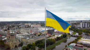 Bayrağın etrafında dalgalanan Ukrayna bayrağı bayrak direğinde destansı bulutlarla. Ukrayna 'nın başkenti Kharkiv' deki Kutsal Annunciation Katedrali 'nin sonbaharda havadan görünüşü