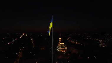 Saat yönünde Ukrayna 'nın parlak sarı ve mavi bayrağı etrafında dalgalanan bayrak direğinde geceleyin. Şehir, Ukrayna 'nın Kharkiv kentindeki Kutsal Annunciation Katedrali ile havadan görüş sağlıyor.