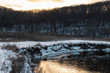 Donmuş nehir kıyısında kış manzarası. Siverskyi Donets Nehri Ukrayna 'da karla kaplıydı. Odunsu tepenin üstündeki bulutlarda gün batımı güneşi