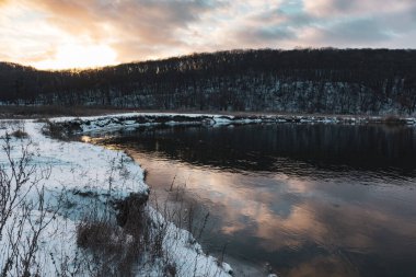 Donmuş nehir kıvrımında kış manzarası manzaralı bulutların yansıması. Siverskyi Donets Nehri üzerindeki Zmiyevsky bölgesi Ukrayna 'da karla kaplıydı. Odunsu tepenin üstündeki bulutlarda gün batımı güneşi