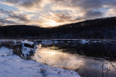 Kış donmuş nehir kıvrımları ve manzaralı güneş yansıması. Siverskyi Donets Nehri üzerindeki Zmiyevsky bölgesi Ukrayna 'da karla kaplıydı. Odunsu tepenin üstündeki bulutlarda gün batımı güneşi