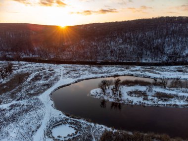 Karlı nehir eğrisinde kış havası. Ukrayna 'nın Siverskyi Donets Nehri üzerindeki Zmiyevsky bölgesi. Odunsu tepenin üzerinde gün batımı güneşi parlıyor