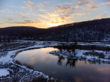 Karlı nehir eğrisinde kışın hava manzarası ve manzaranın yansıması. Ukrayna 'nın Siverskyi Donets Nehri üzerindeki Zmiyevsky bölgesi. Tepenin üstünde güneş batıyor.