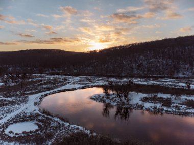 Nehir kıvrımında kışın hava manzarası ve manzaranın yansıması. Ukrayna 'nın Siverskyi Donets Nehri üzerindeki Zmiyevsky bölgesi. Güneşin karlı, ağaçlık tepenin üzerindeki bulutlarda batışı.