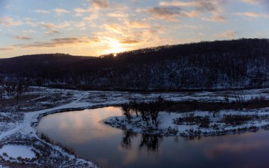 Karlı nehir eğrisinde bulutların yansımasıyla kış havası manzarası. Ukrayna 'nın Siverskyi Donets Nehri üzerindeki Zmiyevsky bölgesi. Odunsu tepenin üstündeki bulutlarda gün batımı güneşi