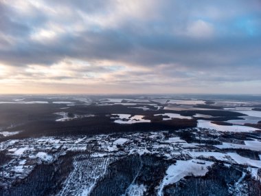 Köye kış destansı hava manzarası, karla kaplı orman ve tarlalar. Ukrayna 'nın Zmiyevsky bölgesi insansız hava aracından. Güneş, ağır gün batımı bulutlarında parlar.