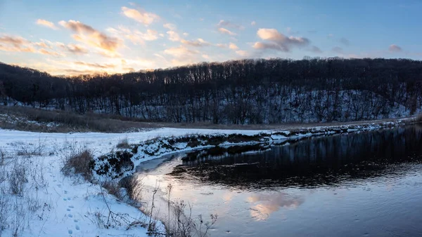 Donmuş nehir eğrisinde manzaralı kış panoramik manzarası. Siverskyi Donets Nehri üzerindeki Zmiyevsky bölgesi Ukrayna 'da karla kaplıydı. Odunsu tepenin üstündeki bulutlarda gün batımı güneşi