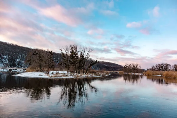 Kış nehri, karlı sahillerde çıplak ağaçların yansıması ve canlı bir akşam bulutlu gökyüzü. Ukrayna 'nın Siverskyi Donets Nehri üzerindeki Zmiyevsky bölgesi