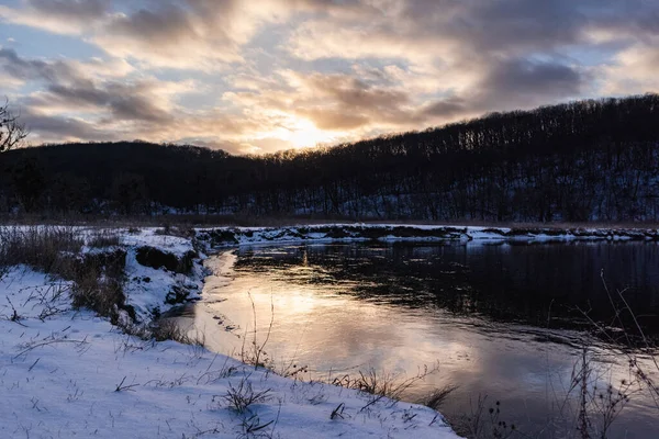 Kış donmuş nehir kıvrımları ve manzaralı güneş yansıması. Siverskyi Donets Nehri üzerindeki Zmiyevsky bölgesi Ukrayna 'da karla kaplıydı. Odunsu tepenin üstündeki bulutlarda gün batımı güneşi