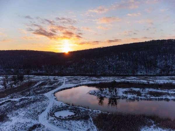Karlı nehir eğrisinde yansımalı kış havası manzarası. Ukrayna 'nın Siverskyi Donets Nehri üzerindeki Zmiyevsky bölgesi. Odunsu tepenin üstündeki bulutlarda gün batımında parlayan güneş