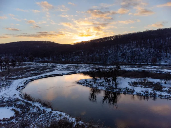 Karlı nehir eğrisinde kışın hava manzarası ve manzaranın yansıması. Ukrayna 'nın Siverskyi Donets Nehri üzerindeki Zmiyevsky bölgesi. Tepenin üstünde güneş batıyor.