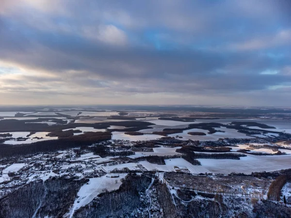 Köyde kış akşamı manzarası, karla kaplı orman ve tarlalar. Ukrayna 'nın Zmiyevsky bölgesi insansız hava aracından. Soğuk kırsal arazinin üzerindeki mor renkli bulutlar