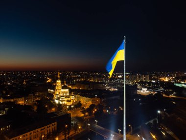 Ukrayna 'nın parlak sarı ve mavi bayrağını dalgalandır gece bayrak direğinde sallayarak. Şehir, Ukrayna 'nın Kharkiv kentindeki Kutsal Annunciation Katedrali ile havadan görüş sağlıyor.
