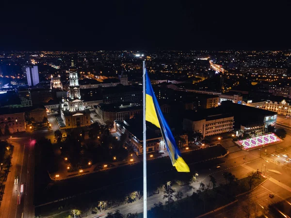 Ukrayna 'nın aydınlanmış bayrağı karanlık gece şehir manzarasında dalgalanıyor. Ukrayna 'nın Kharkiv kentindeki Dormition Katedrali yakınlarındaki şehir merkezi hava manzarası