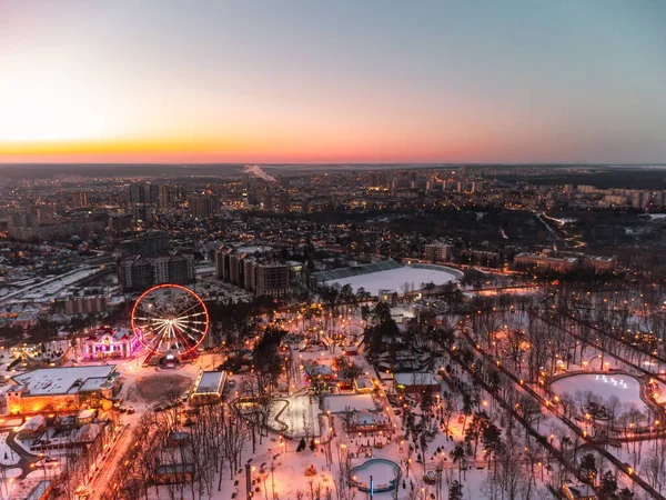 Havadan canlı akşam manzarası, dönme dolap ve kışın beyaz karla kaplı eğlenceler. Günbatımı renkleriyle Kharkiv şehir merkezi, eğlence Gorky Central Park