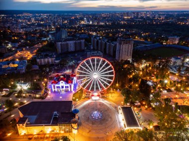 Hava parlaklığı, çeşme ve cazibeyle dönme dolabı aydınlattı. Kharkiv şehir merkezi dinlenme alanı akşam ışıkları altında. Gün batımında Gorky Central Park