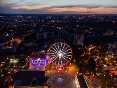 Havadan aydınlatılmış dönme dolap. Kharkiv şehir merkezi dinlenme alanı akşam ışıkları altında. Gökyüzünden günbatımında Gorky Central Park