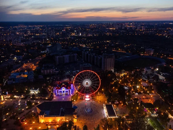 Havadan aydınlatılmış dönme dolap. Kharkiv şehir merkezi dinlenme alanı akşam ışıkları altında. Gün batımında Gorky Central Park