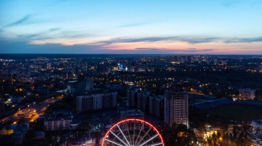 Canlı akşam şehir manzarasına hava manzarası, gün batımında dönme dolabın çekildiği şehir binaları. Günbatımı renklerinde Kharkiv şehir merkezi, Ukrayna