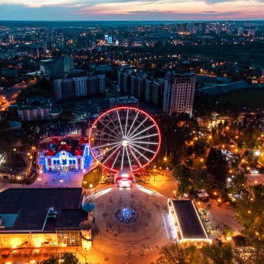 Havadan aydınlatılmış dönme dolap ve diğer gösteriler. Kharkiv şehir merkezi dinlenme alanı akşam ışıkları altında. Gün batımında Gorky Central Park