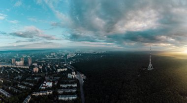 Güneşin doğuşuyla birlikte gökyüzü bulutlu ve güneşli, yerleşim bölgesi yakınlarındaki ormandaki telekomünikasyon kulesiyle hava manzarası. Kharkiv, Ukrayna