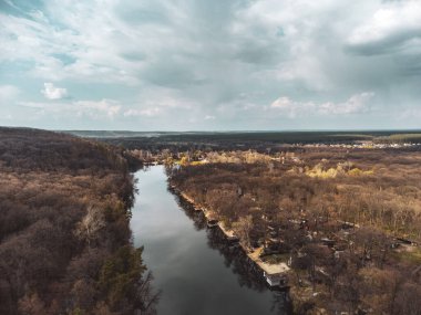 Aerial view on river curve in bare trees forest with epic cloudy sky. Nature landscape from drone near Koropove village in Kharkiv region. Color graded
