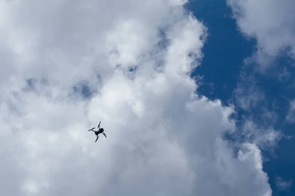 Drone quadrocopter silhouette flying high in white clouds on blue sky, cloudscape background. Skyscape scenery