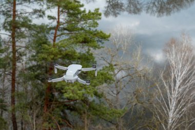 Kharkiv, Ukraine - April 22, 2021: Dji Mavic Mini 2 drone, flying in sunny pine forest on scenic river bank, back view. Quadcopter hovering with background blur