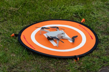 Kharkiv, Ukraine - April 22, 2021: Dji Mavic Mini 2 drone on orange landing mat platform. Quadcopter on nylon foldable launch pad placed in green grass with ground nails. Accessories for safe landing