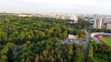 Aerial, flying backwards view of Kharkiv city center streets near Gorky Park, stadium and residential multistory buildings with scenic sunset in summer