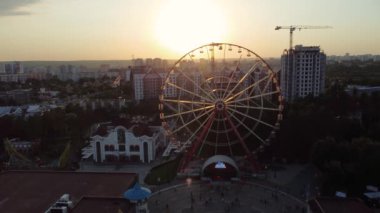 Aerial dolly footage of ferris wheel spinning at sunset, push-in view in Kharkiv city center, amusement Park of Maxim Gorky. High attraction for recreation and city observation