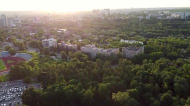 Sunny greenery in city park district, aerial rising up view from drone. Recreation area in Kharkiv near residential buildings in sunset