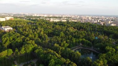 Aerial fpv drone backwards flying view on attractions and recreation area in greenery in sunset light. Evening view in Kharkiv city center Gorky Park