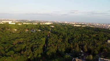 Cable car attraction in green forest, aerial flying forward view in summer Kharkiv city recreation park at sunset