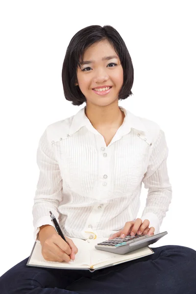 Junge asiatische Geschäftsfrau hält Taschenrechner in der Hand und schreibt Leistung ins Notizbuch — Stockfoto