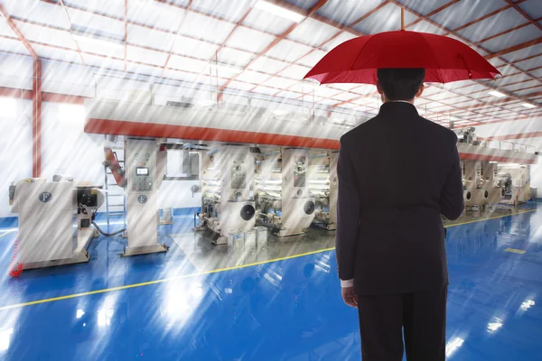Businessman with an umbrella standing against the background of production — Stock Photo, Image