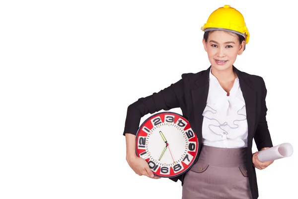 Female engineer in a yellow hard hat holding a drawing and a large clock — Stock Photo, Image