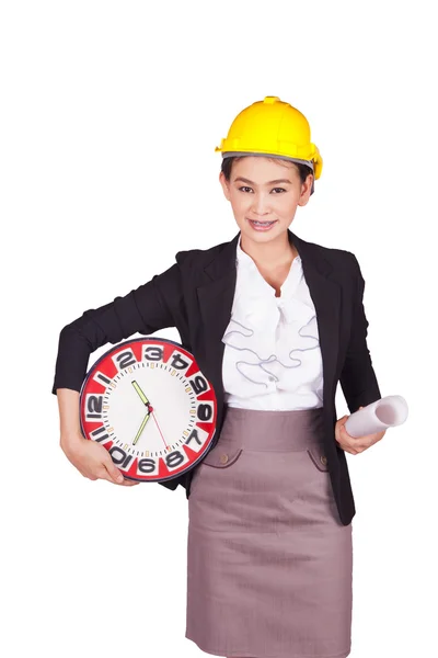 Female engineer in a yellow hard hat holding a drawing and a large clock — Stock Photo, Image
