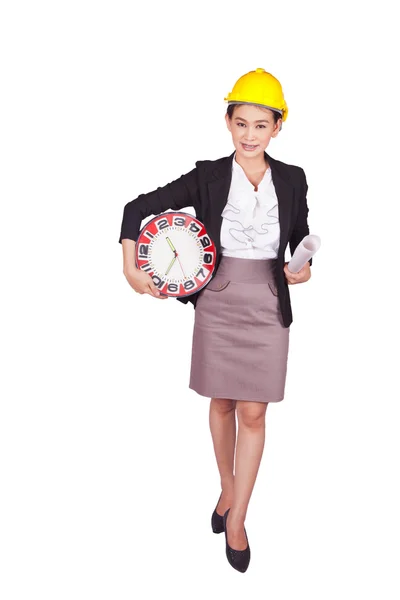 Female engineer in a yellow hard hat holding a drawing and a large clock — Stock Photo, Image